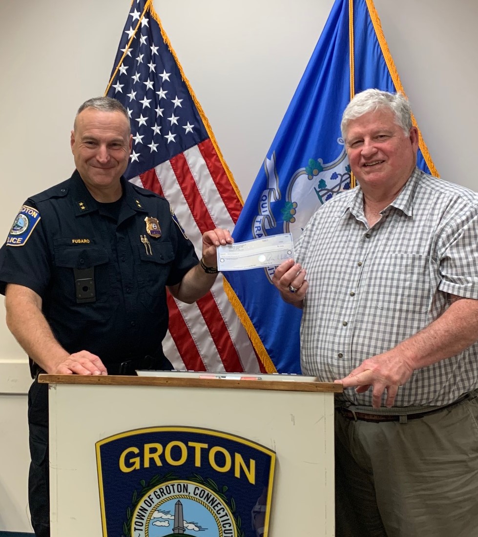 A chief of police in uniform presenting a check to a man in front of American flag