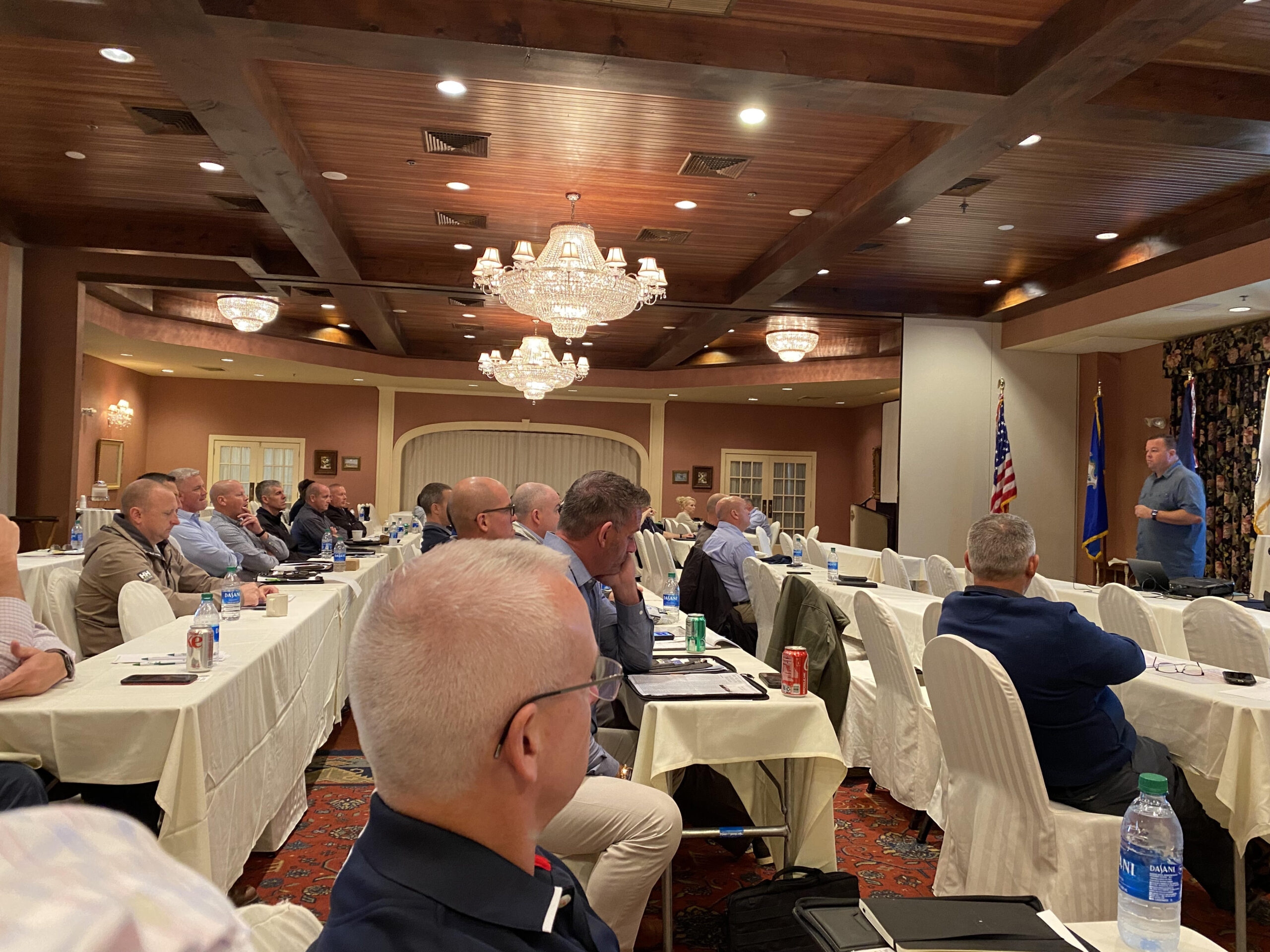 men seated at tables listening to speaker presentation